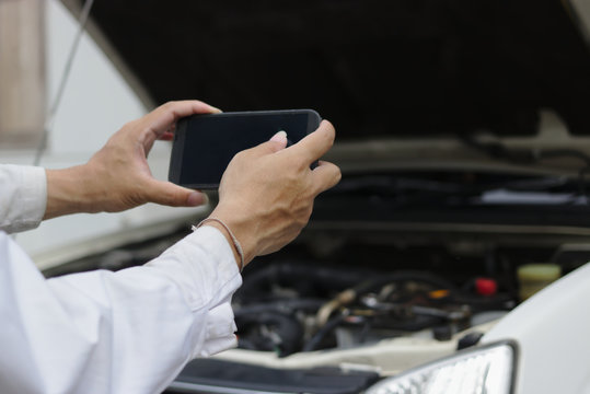 Hands of mechanic man taking a picture with mobile smart phone against car in open hood at the repair garage.