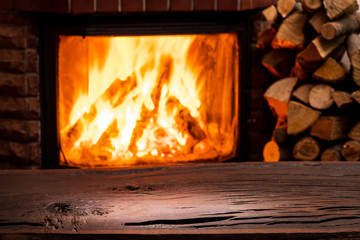 Obraz premium Empty wooden table and fireplace with warm fire at the background.