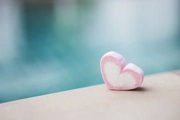 Pink heart marshmallow on swimming pool edge over blurred blue background