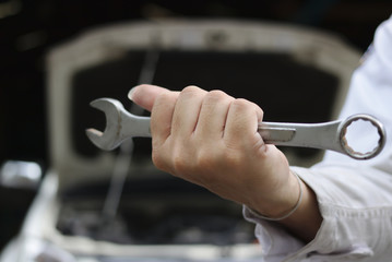 Close up hands of professional young mechanic man holding wrench with open hood at the repair garage. Car insurance concept.