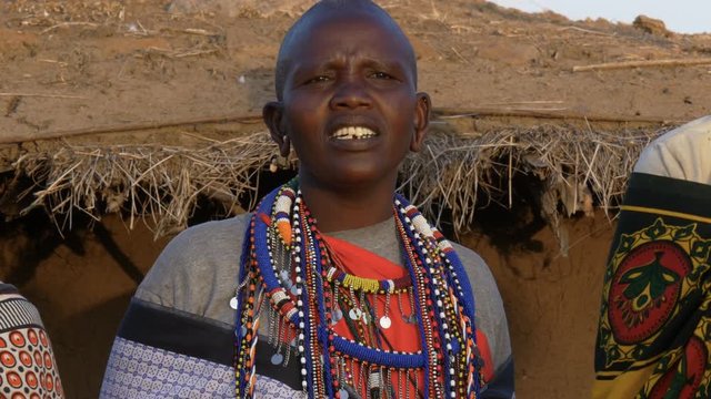 close up of a maasai woman wearing grey clothing and traditional jewellery singing in a village near masai mara in kenya