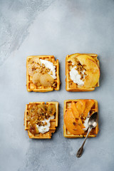 Delicious Belgian wafers with caramelized fruit, apple, banana, persimmon, pear and walnuts on a gray concrete or stone background. Ideas for breakfast. Selective focus. Top view. Place for text.