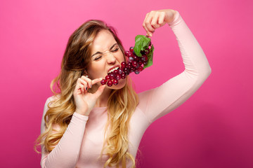 Funny woman eating grape on pink background