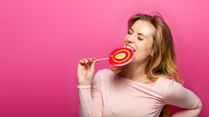 Beautiful young woman with big lollipop on pink background