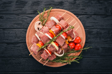 Raw kebab from meat on a wooden background with vegetables. Top view. Free space for text.