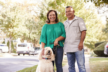 Portrait Of Senior Couple Walking Dog Along Suburban Street - Powered by Adobe