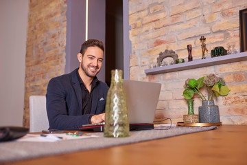 A happy handsome young businessman using a laptop in office environment.