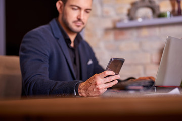A serious handsome young businessman using his smartphone in office environment.