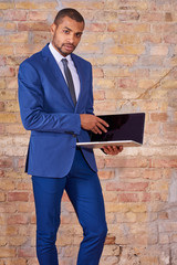 A serious handsome young businessman pointing to the screen of his laptop in a suit.