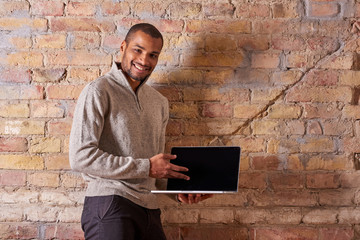 A happy handsome young man pointing to the screen of his laptop in a sweater.