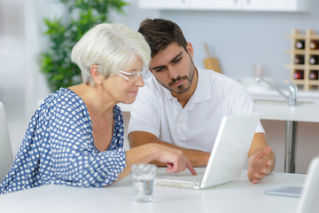 Fototapeta premium Young man helping senior lady to use a laptop