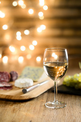 glass of white wine with french cheese and delicatessen in restaurant wooden table with romantic dim light and cosy atmosphere
