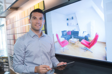 Man stood by screen showing image of a lounge area