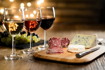 Foto op Plexiglas drie glazen rode wijn, rose wijn en witte wijn met Franse kaas en delicatessen in restaurant houten tafel met romantisch gedimd licht en gezellige sfeer © W PRODUCTION