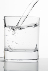 Water being poured into a glass. And water glass with reflection on white background.
