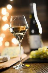 glass of white wine with french cheese and delicatessen in restaurant wooden table with romantic dim light and cosy atmosphere