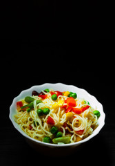 Instant noodles with mixed vegetables in the bowl on dark wooden background with copy space.