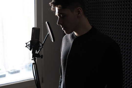 Close-up portrait of a young man standing in profile with a microphone stand in front of the window