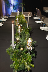 Close up glasses, forks, knives, napkins, candles and decorative flower on dark black tablecloth on table served for dinner in cozy restaurant. Empty served restaurant table with plates and wine glass