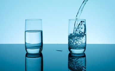 Creative splashing water in the glass on blue background.