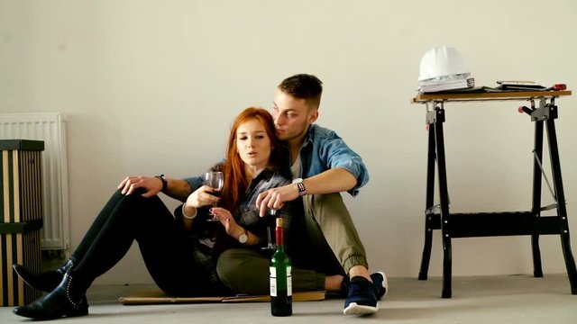 Young, happy couple talking and drinking wine on floor at their new home 
