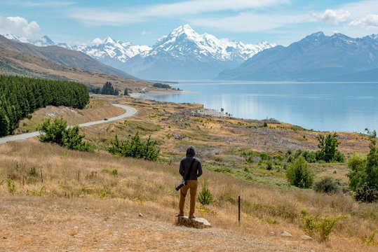 Young male photographer in hoody watching at Mount Cook, one of the most famous snowy mountain at peter&rsquo;s lookout in South Island, New Zealand. Travel in summer concept