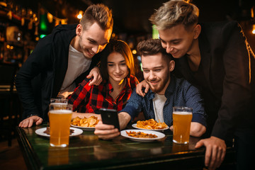 Fun company watches photo on phone in a sport bar