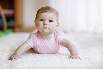 Portrait of baby girl in white sunny bedroom. Newborn child learning crawling.