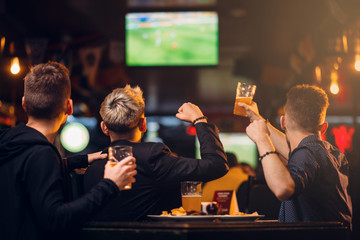Three men watches football on TV in a sport bar - obrazy, fototapety, plakaty