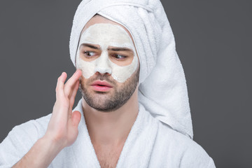man in bath robe and towel with clay mask on face, isolated on grey, skin care concept