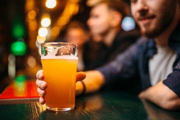 Male person holds glass with beer at bar counter