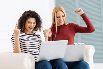Lets celebrate. Delighted brunette with curly hair opening mouth and bowing head while looking at computer