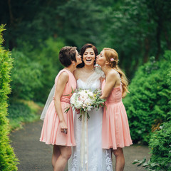 Laughing bride and bridesmaids tell funny stories standing in the park