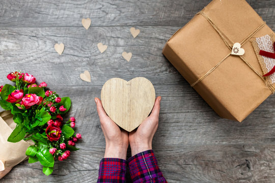 Female hand holding a wooden heart, Valentine's Day, romantic photos . with a gift and a bouquet of flowers, with hearts and gifts, suitable for advertising