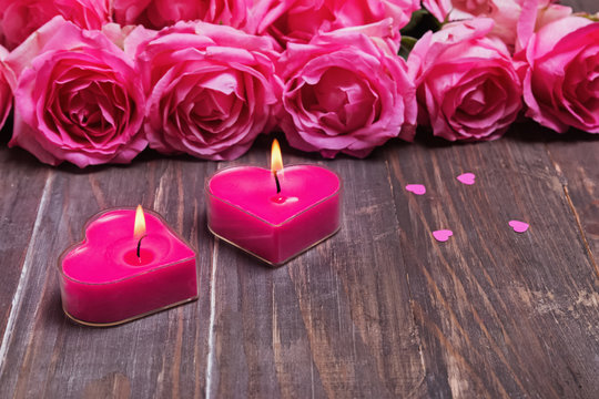 Two burning candles and beautiful pink roses on the wooden background