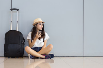 Asian woman teenager using smartphone at airport terminal sitting with luggage suitcase and...