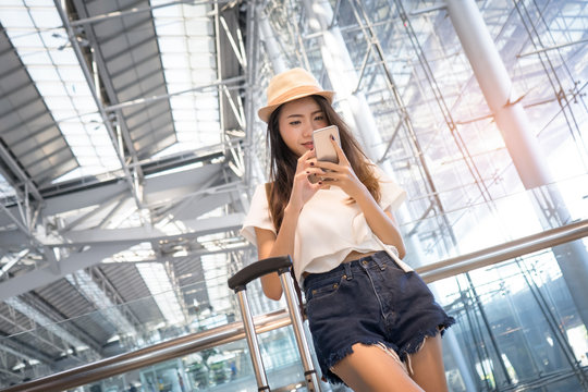 Asian woman teenager using smartphone at airport terminal with luggage suitcase and backpack for travel in vacation summer relaxing waiting flight transport online check in or booking ticket