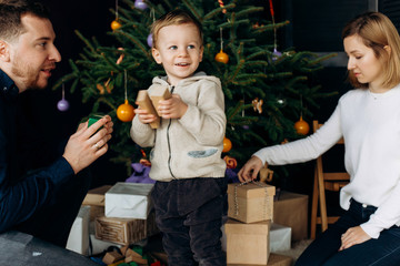 Happy parents play with little son before a New Year tree