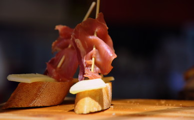 Leckere Tapas mit Schinken und Käse auf Baguette und Holzbrett