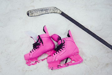 pink skates and hockey stick lie on the snow