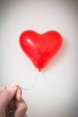 Obraz premium Male hand holding a red heart shaped balloon