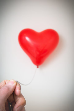 Male hand holding a red heart shaped balloon