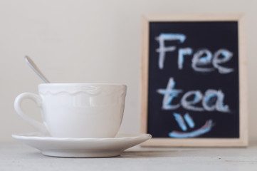 White cup with tea standing near blackboard sign with promotion 