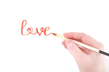 Hand writing the word Love (with one of the letters shaped as a heart) with a brush and red watercolor paint on white paper, top view