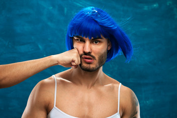 Unidentified male hand beating the face of pretty cross dressing man wearing blue wig and glasses