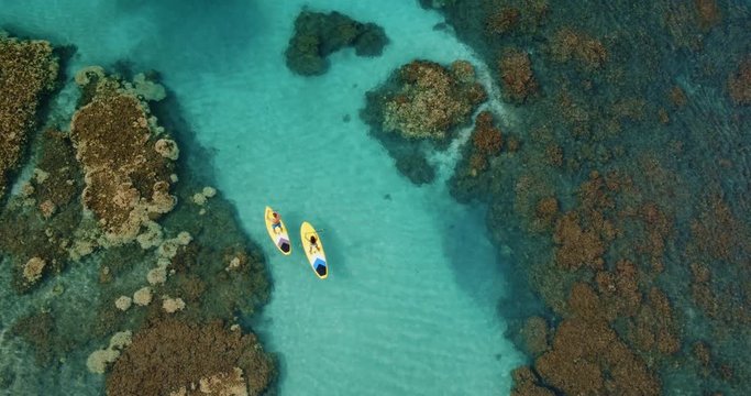 Cinematic aerial view of couple stand up paddling across tropical reef