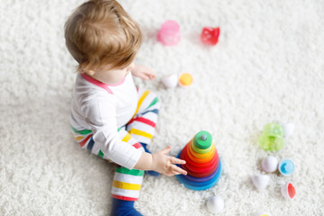 Fototapeta na wymiar Adorable cute beautiful little baby girl playing with educational colorful wooden rainboy toy pyramid
