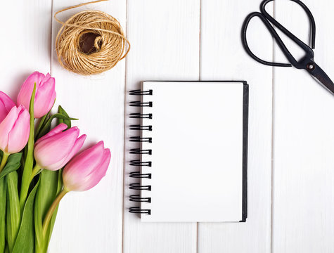 Blank paper notepad and pink tulips on the white wooden table