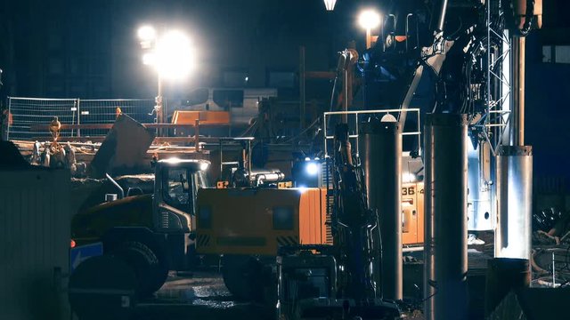 Drilling wells for piling building piles on a construction site at night with a lot of construction equipment 