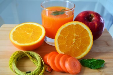 Fresh fruits , tape measure and a glass of orange juice on a wooden board.